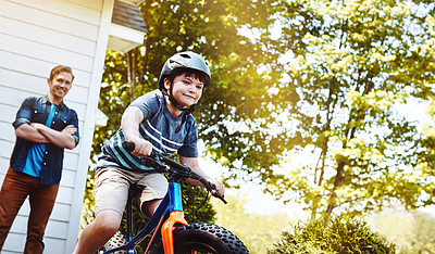 Buy stock photo Shot of a young boy riding a bicycle with his father in the background