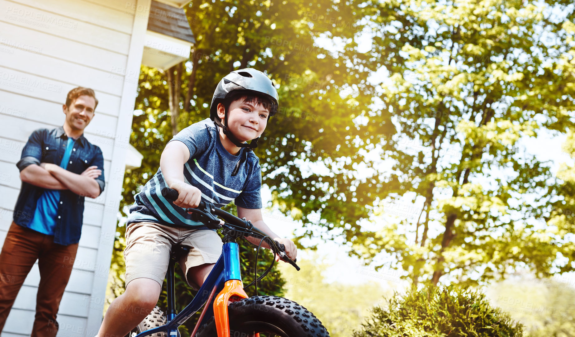 Buy stock photo Shot of a young boy riding a bicycle with his father in the background