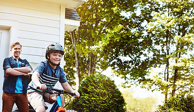 Buy stock photo Shot of a young boy riding a bicycle with his father in the background