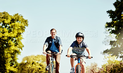 Buy stock photo Shot of a young boy and his father riding together on their bicycles