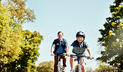 Buy stock photo Shot of a young boy and his father riding together on their bicycles