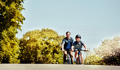 Buy stock photo Shot of a young boy and his father riding together on their bicycles