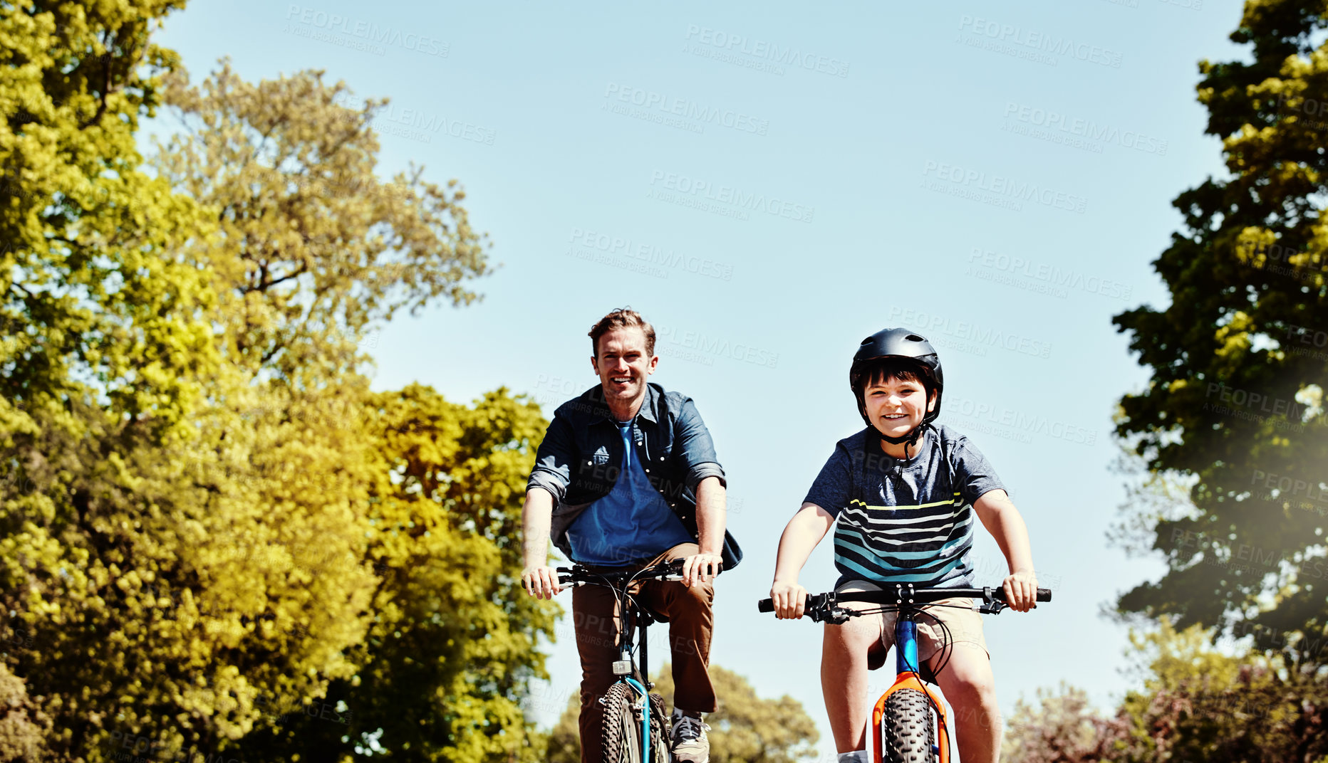 Buy stock photo Shot of a young boy and his father riding together on their bicycles