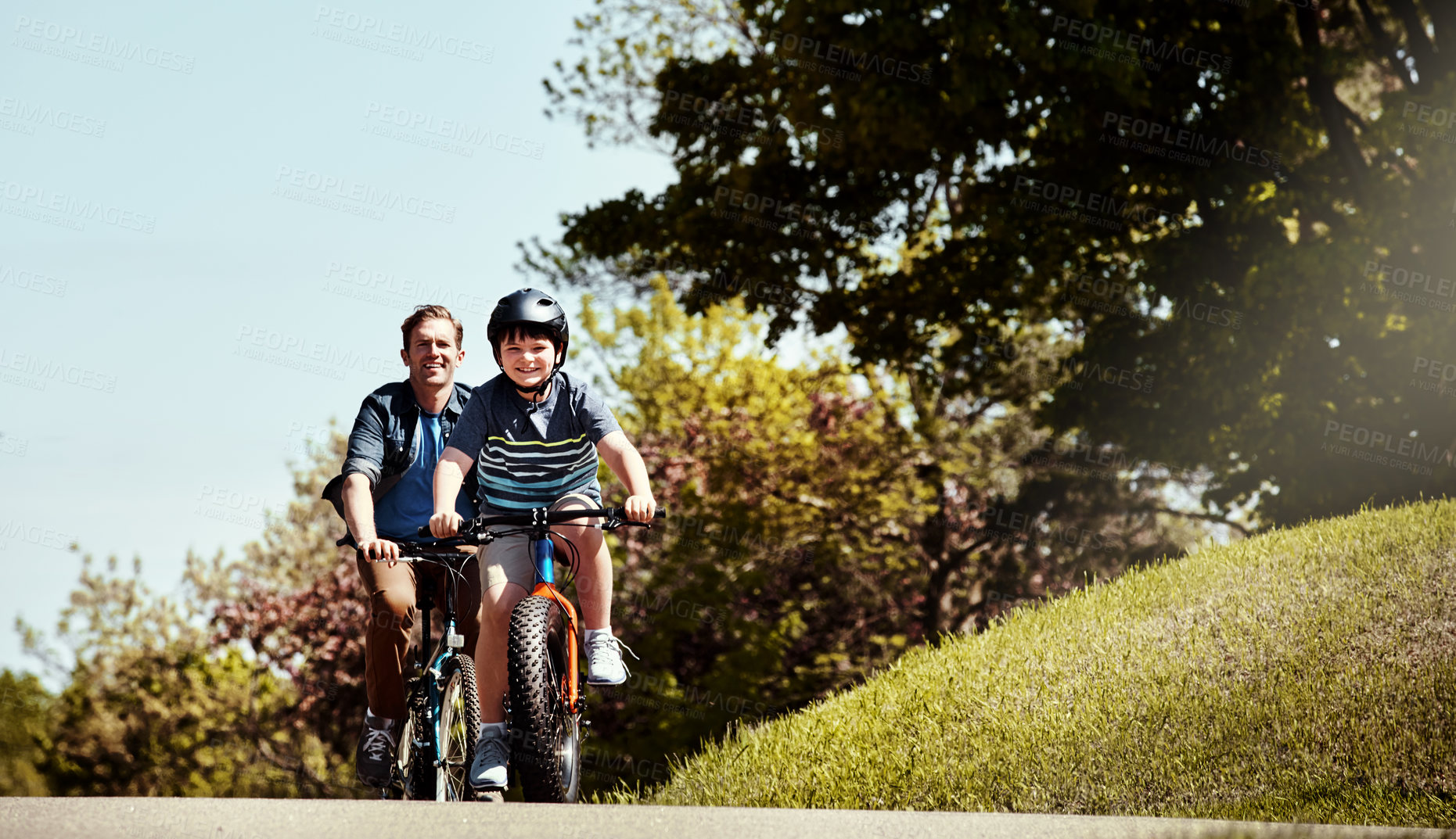 Buy stock photo Shot of a young boy and his father riding together on their bicycles