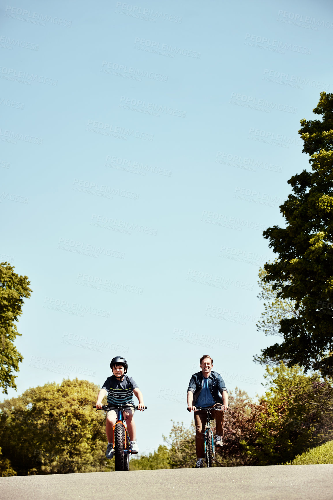 Buy stock photo Shot of a young boy and his father riding together on their bicycles