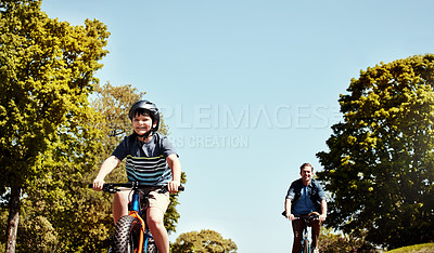 Buy stock photo Shot of a young boy and his father riding together on their bicycles