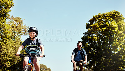 Buy stock photo Shot of a young boy and his father riding together on their bicycles