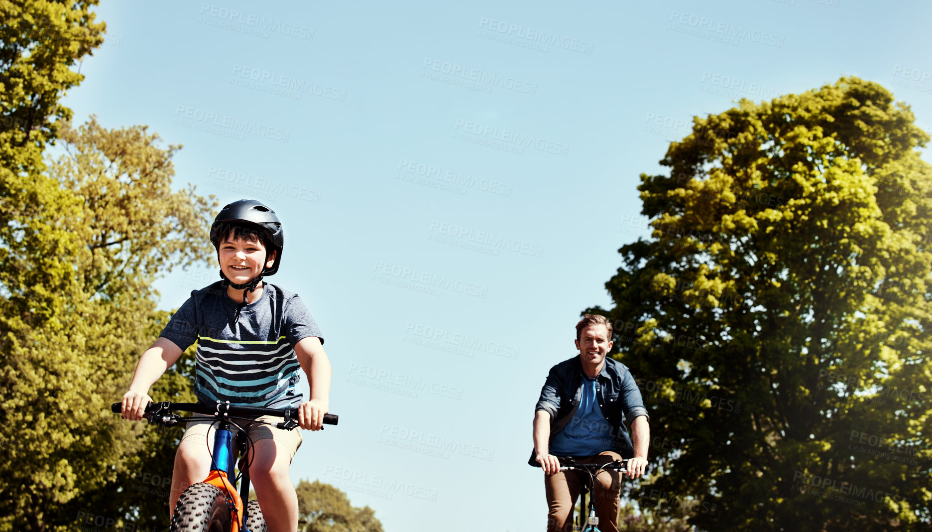 Buy stock photo Shot of a young boy and his father riding together on their bicycles