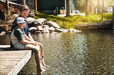 Buy stock photo Shot of a father and his little son sitting on a pier at a lake