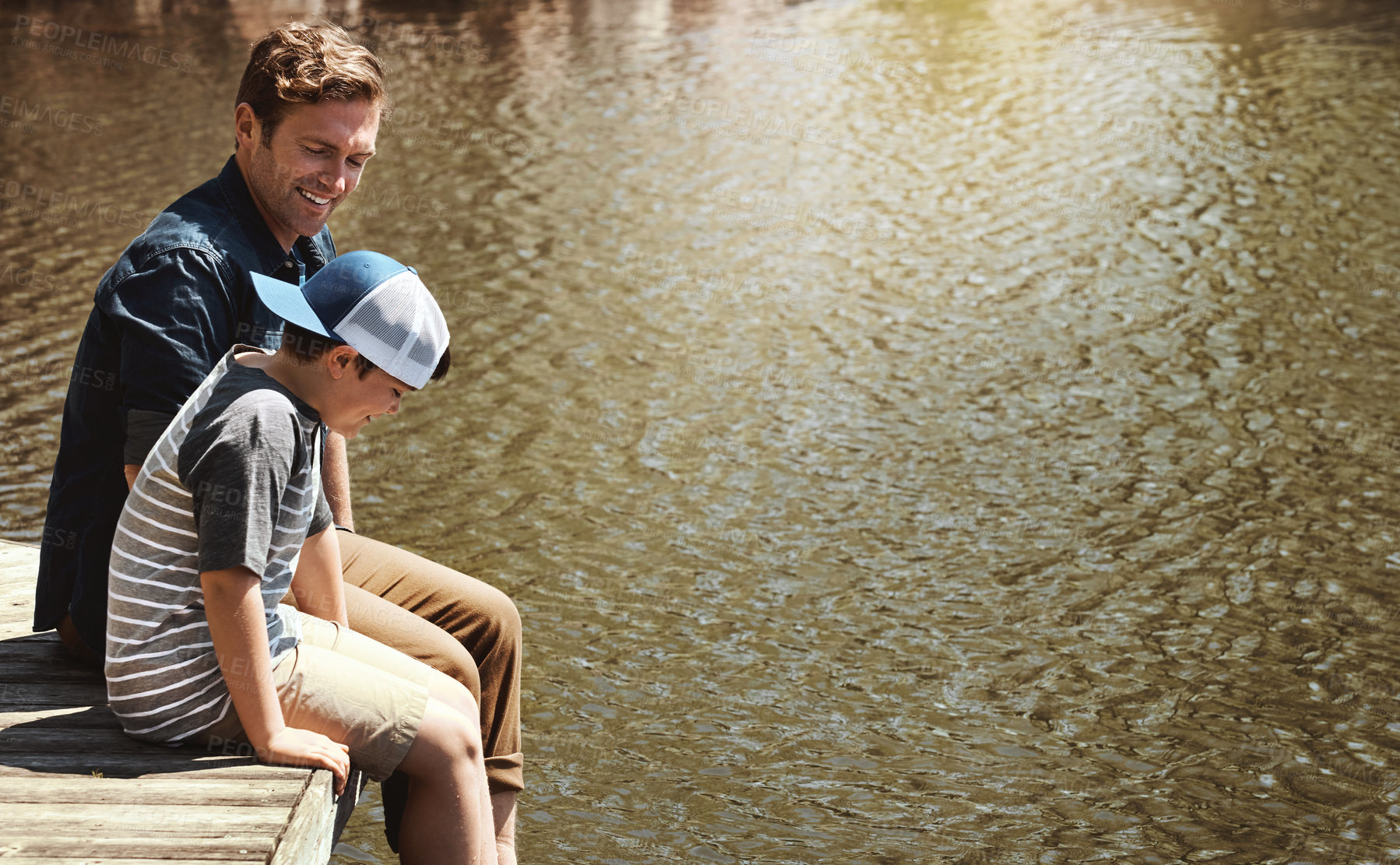 Buy stock photo Shot of a father and his little son sitting on a pier at a lake