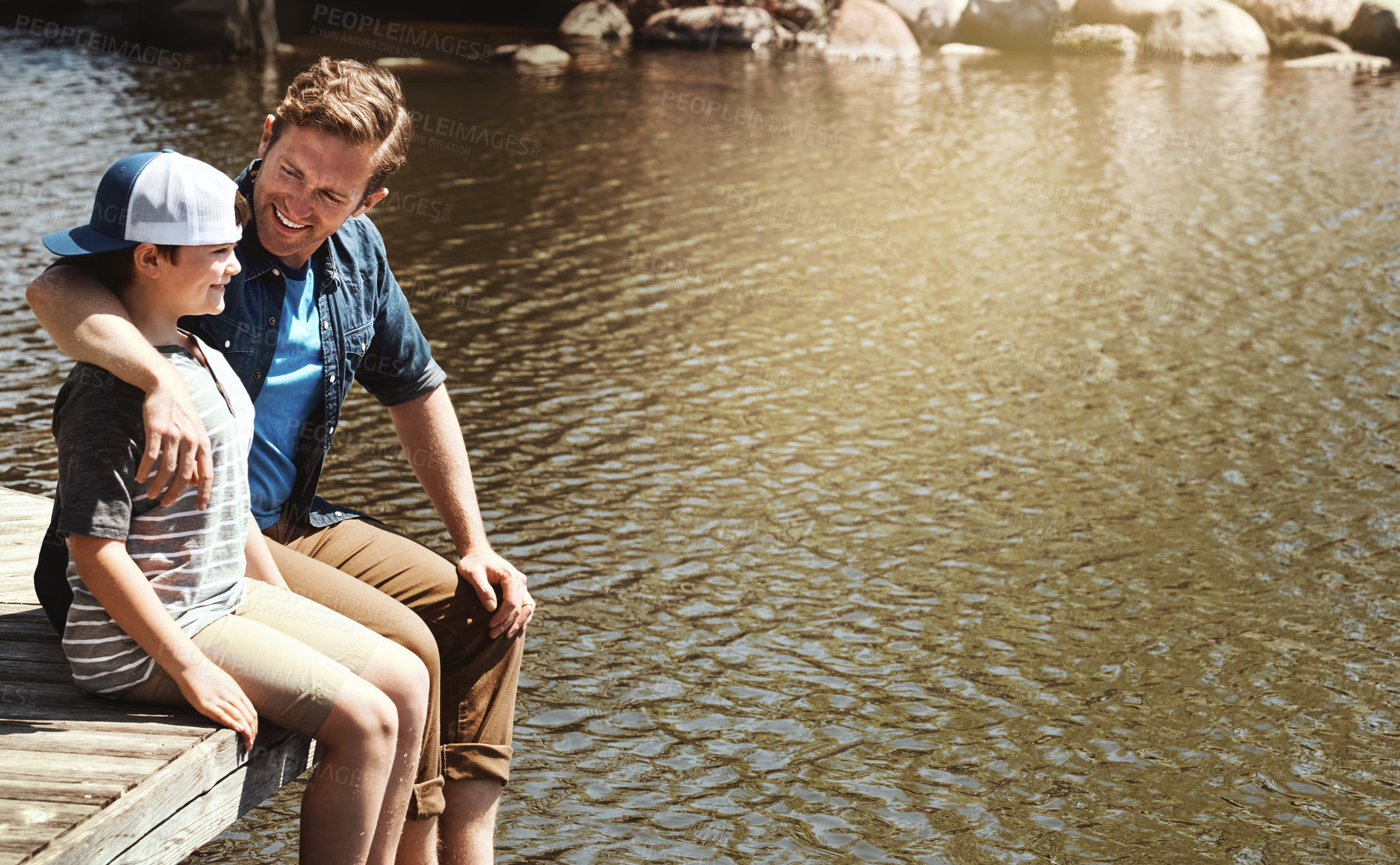 Buy stock photo Shot of a father and his little son sitting on a pier at a lake