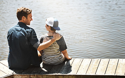 Buy stock photo Rear view shot of a father and his little son sitting on a pier at a lake