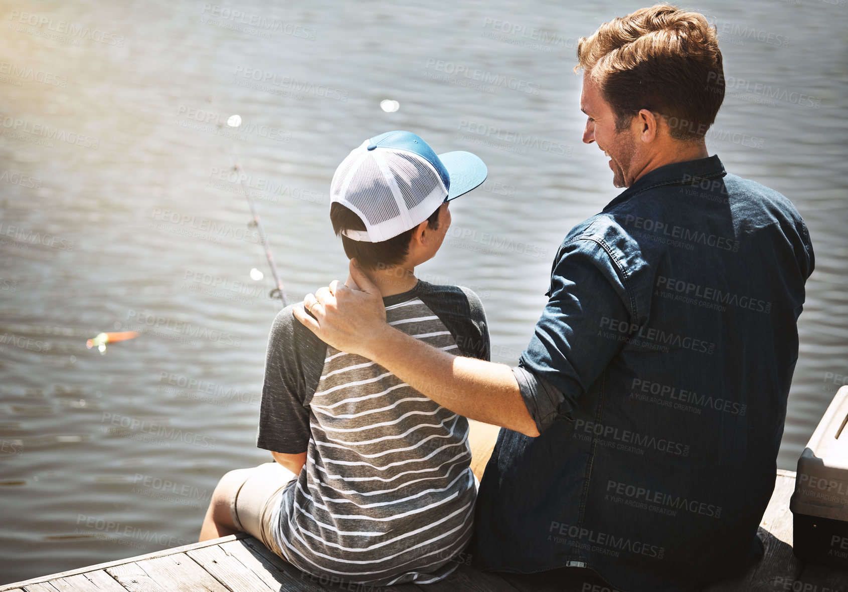 Buy stock photo Happy father, back and teaching son with fishing rod by lake, ocean or beach together in nature. Dad with young child, kid or little boy with hug for lesson or tips to catch sea creatures by water