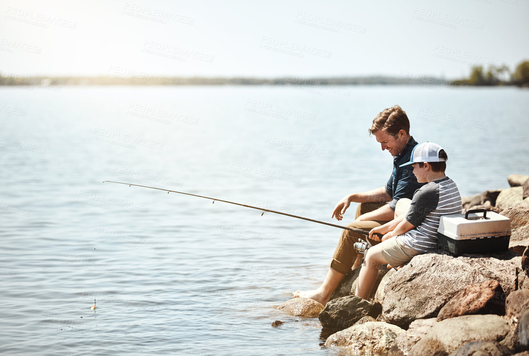 Buy stock photo Happy father, son and fishing on rock with rod by lake, ocean or beach together in nature. Dad with child, young kid or little boy with smile for bonding, lesson or teaching tip to catch by sea water