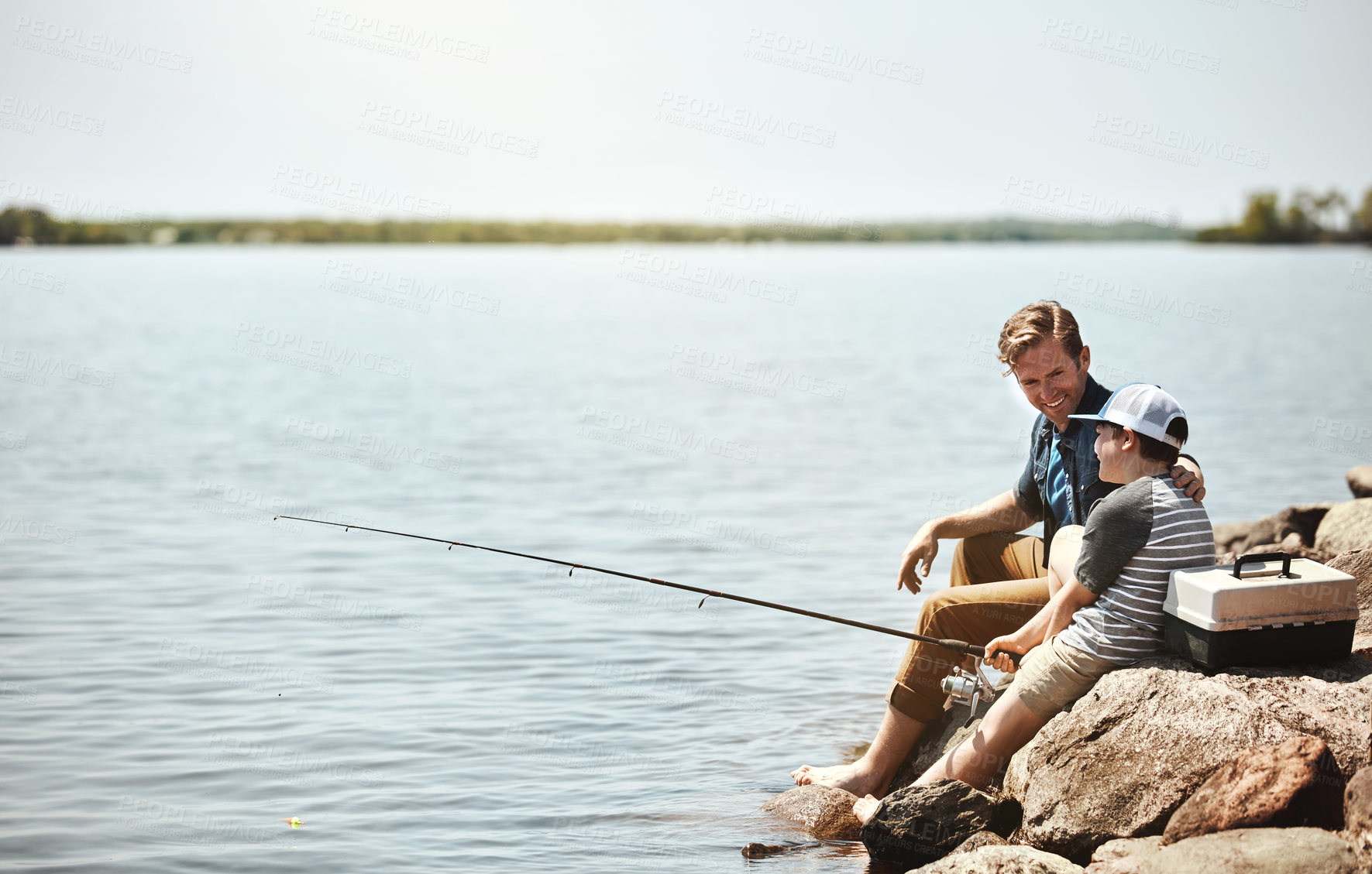 Buy stock photo Happy father, child and fishing on rock with rod by lake, ocean or beach together in nature. Dad with son, young kid or little boy with smile for bonding, lesson or teaching tip to catch by sea water