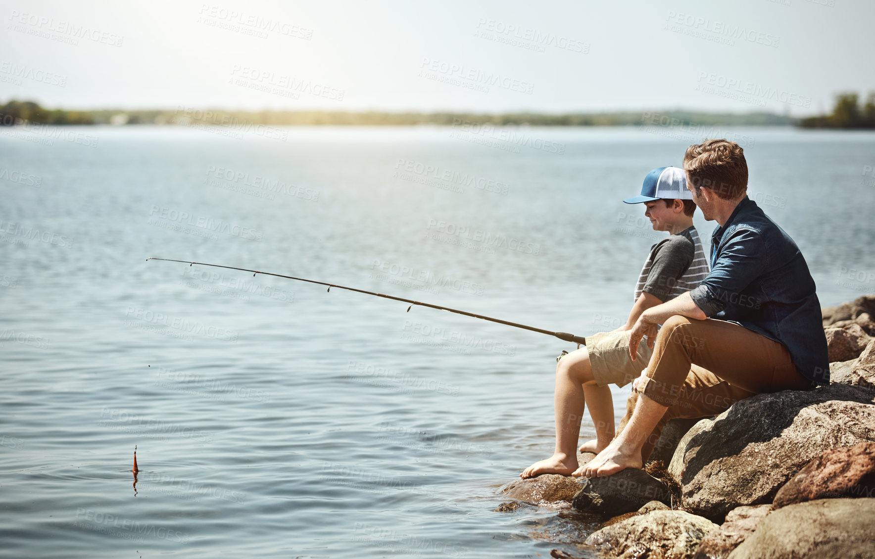 Buy stock photo Happy dad, son and fishing with rod on rock by lake, ocean or beach together in nature. Father with kid, young child or little boy for bonding, teaching tips or lesson to catch by sea water or coast