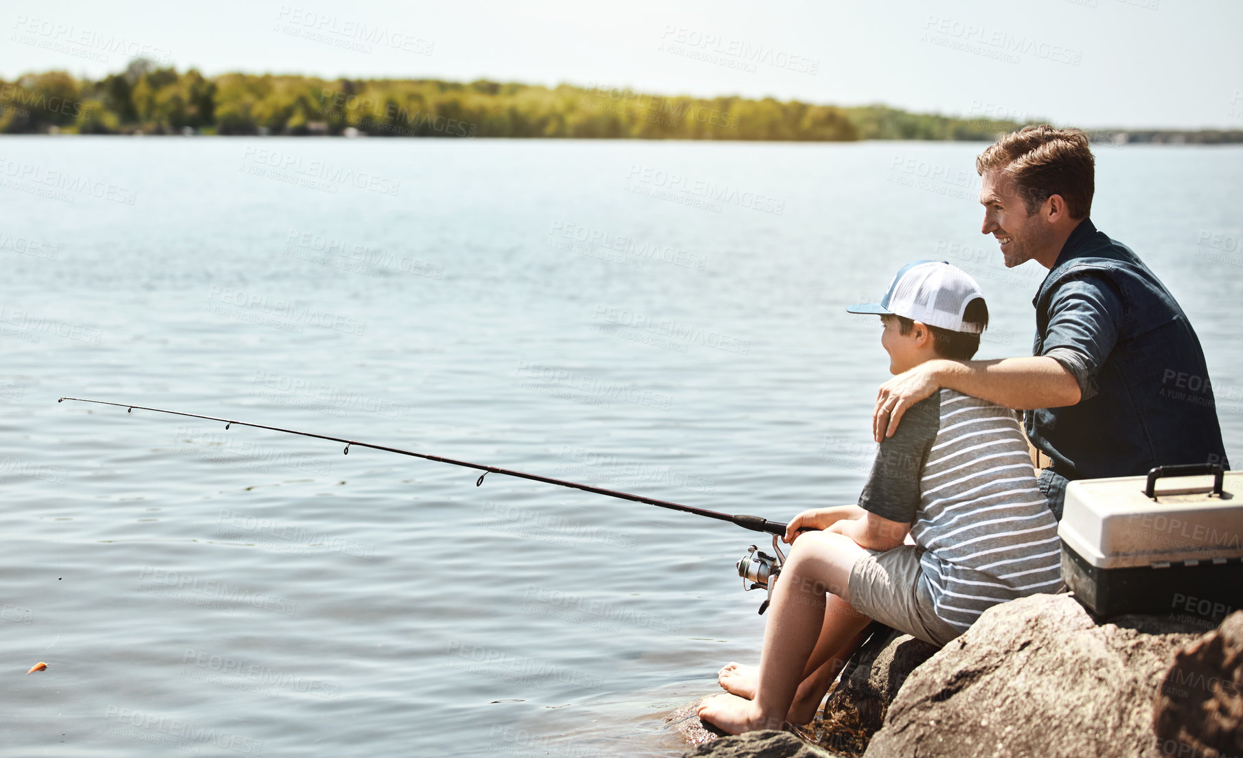 Buy stock photo Happy father, fishing and teaching with son on rock with rod by lake, ocean or beach together in nature. Dad with kid, young child or little boy for bonding, lesson or tips to catch by sea water