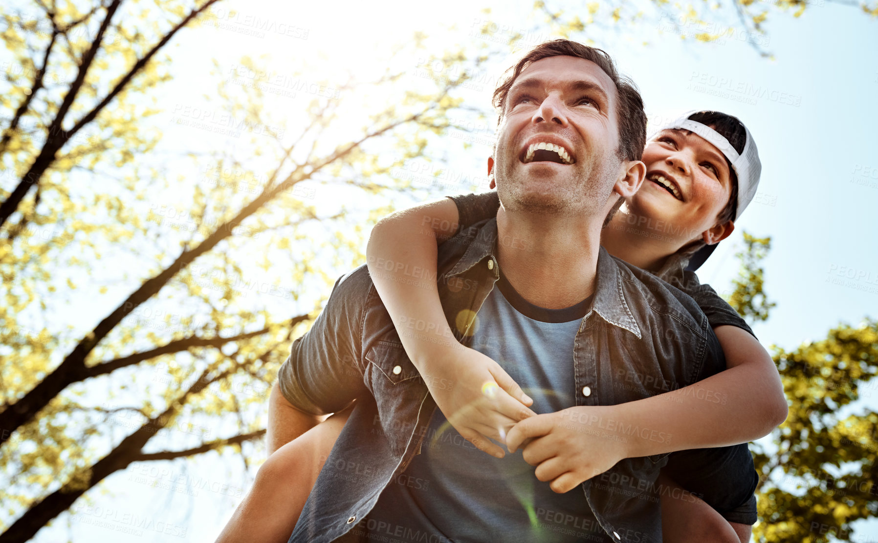 Buy stock photo Low angle shot of a father giving his little son a piggyback ride outdoors