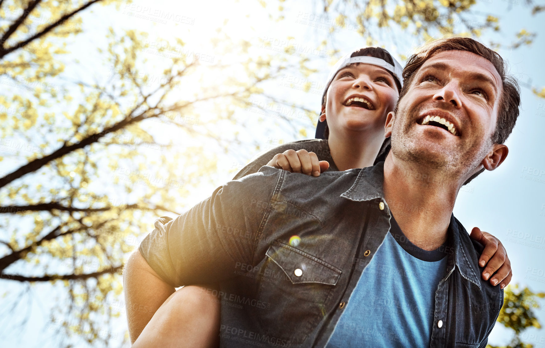 Buy stock photo Low angle shot of a father giving his little son a piggyback ride outdoors