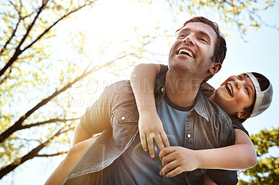 Buy stock photo Low angle shot of a father giving his little son a piggyback ride outdoors