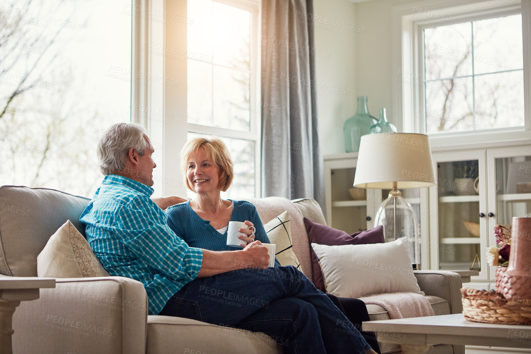 Buy stock photo Senior couple, coffee and happy on couch in conversation, relax and talking in home living room. Old man, elderly woman and smile for bonding with care, love and chat in retirement on sofa in house