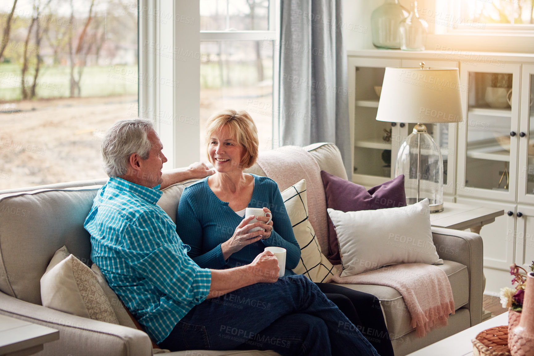 Buy stock photo Senior couple, coffee and happy on sofa in conversation, relax and memory in home living room. Old man, elderly woman and smile for bonding with care, love and story in retirement on couch in house