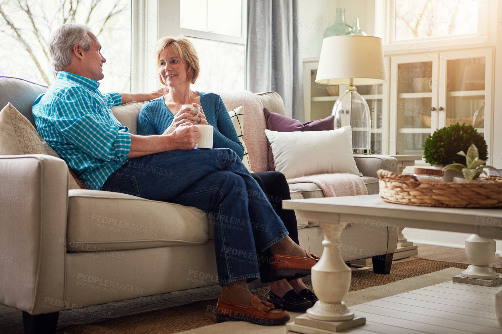 Buy stock photo Senior couple, coffee and smile on sofa in conversation, relax or happy memory in home living room. Old man, elderly woman and chat for bonding with tea, love or story in retirement on couch in house