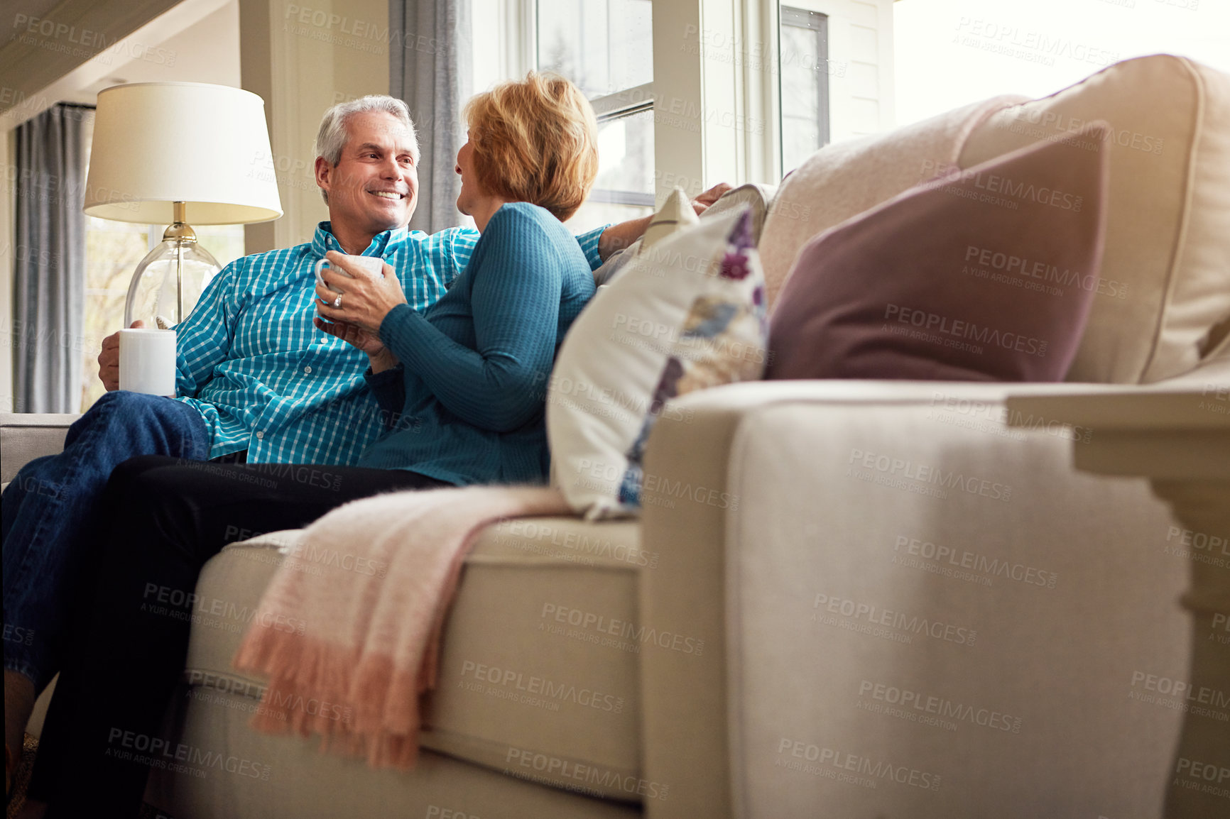 Buy stock photo Senior couple, tea and smile on sofa in conversation, relax or happy memory in home living room. Old man, elderly woman and chat for bonding with coffee, love or story in retirement on couch in house