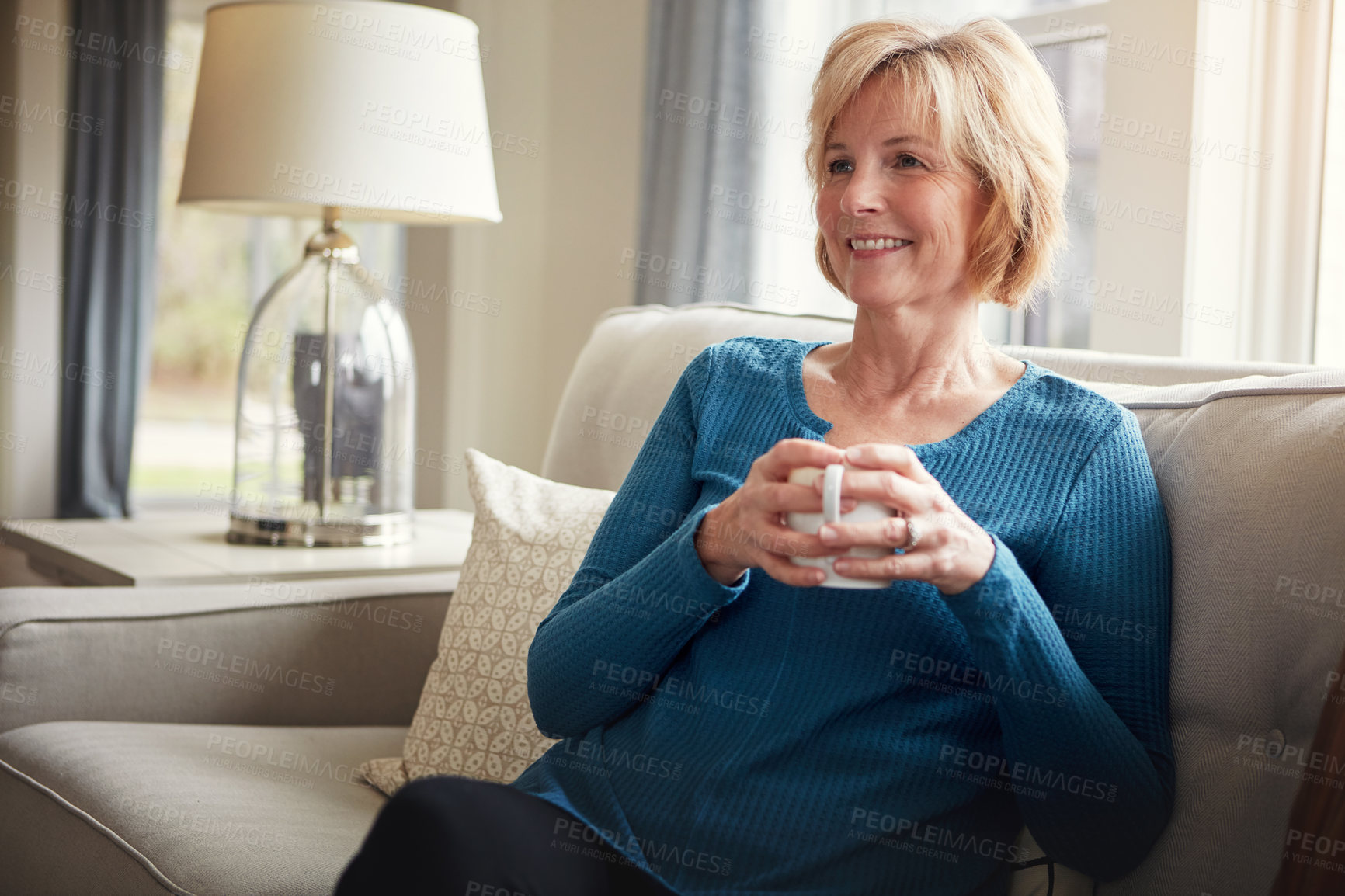 Buy stock photo Shot of a happy mature woman relaxing on the sofa with a warm beverage at home