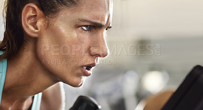 Buy stock photo Cropped shot of a determined looking young woman working out on an elliptical machine in the gym