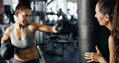 Buy stock photo Cropped shot of a young female boxer working out on a punching bag with her trainer in the gym