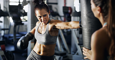 Buy stock photo Cropped shot of a young female boxer working out on a punching bag with her trainer in the gym