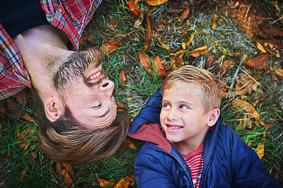 Buy stock photo High shot portrait of a handsome young man and his son lying on the grass outside during autumn