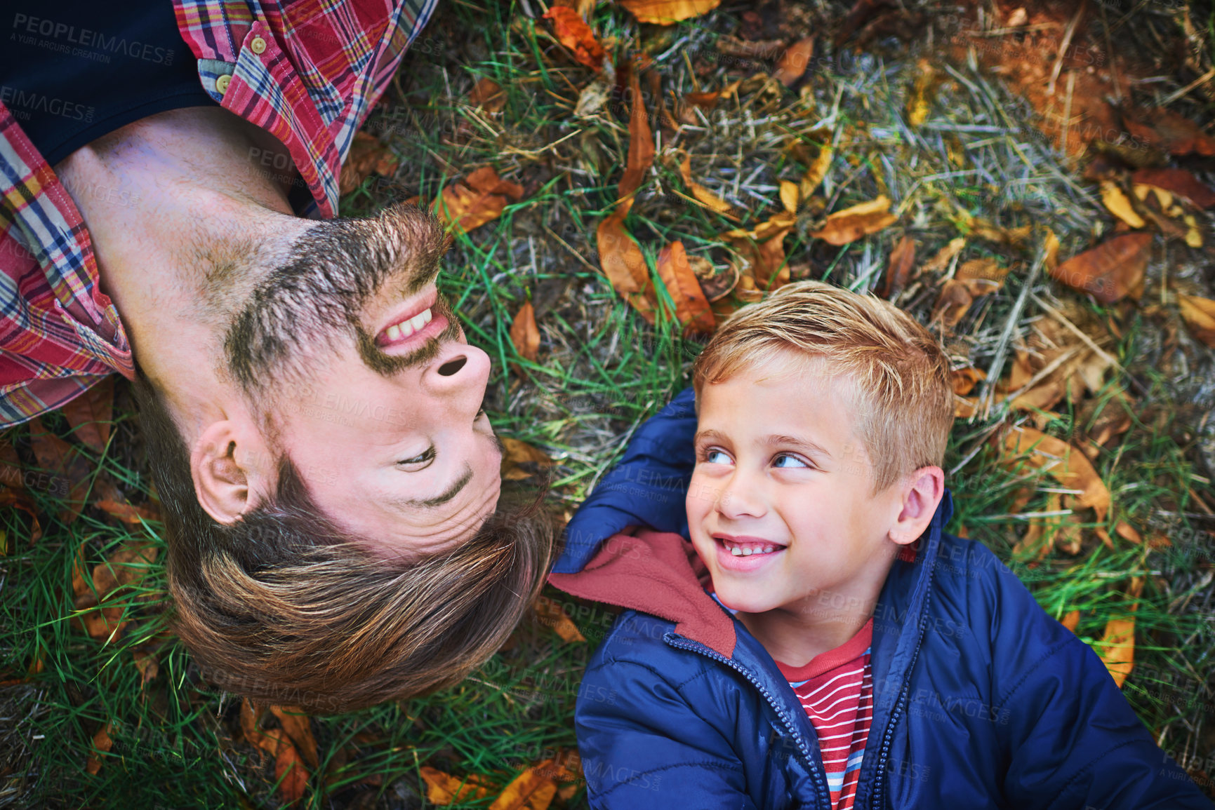 Buy stock photo High shot portrait of a handsome young man and his son lying on the grass outside during autumn
