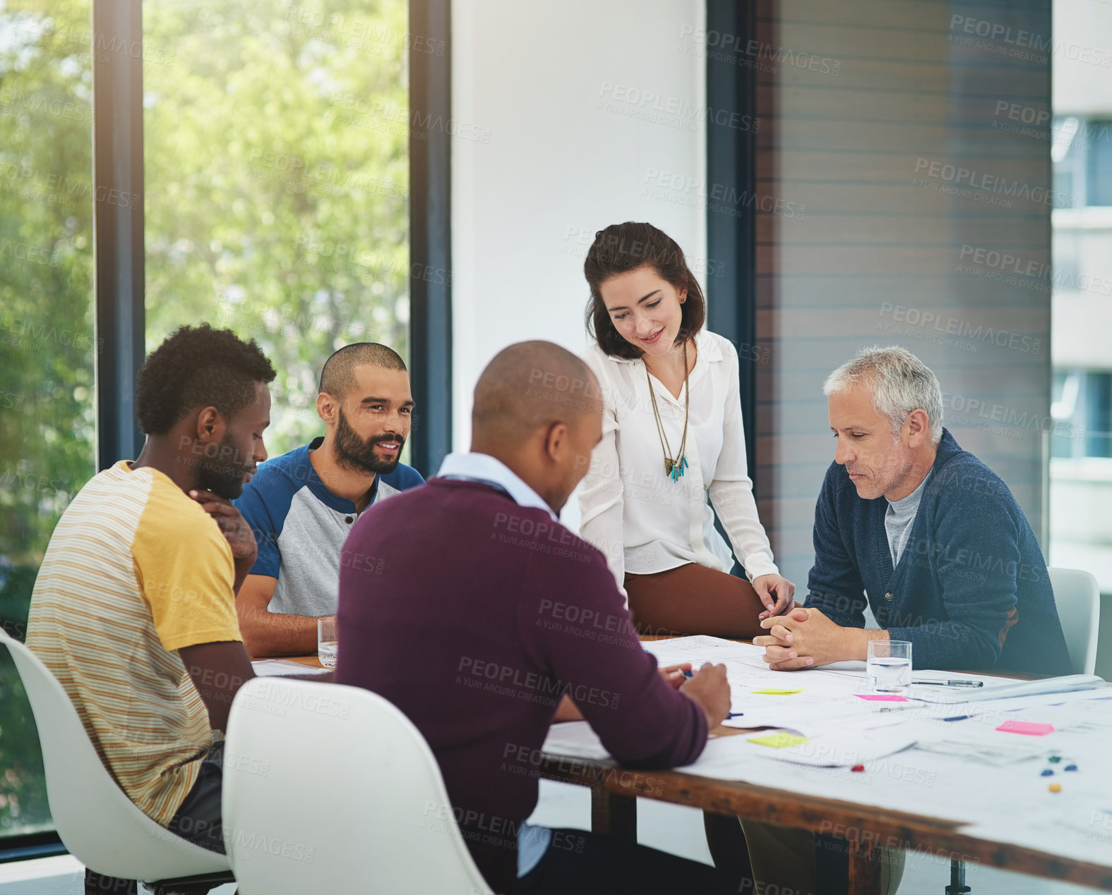 Buy stock photo Cropped shot of a group of architects looking over blueprints during a meeting in the boardroom