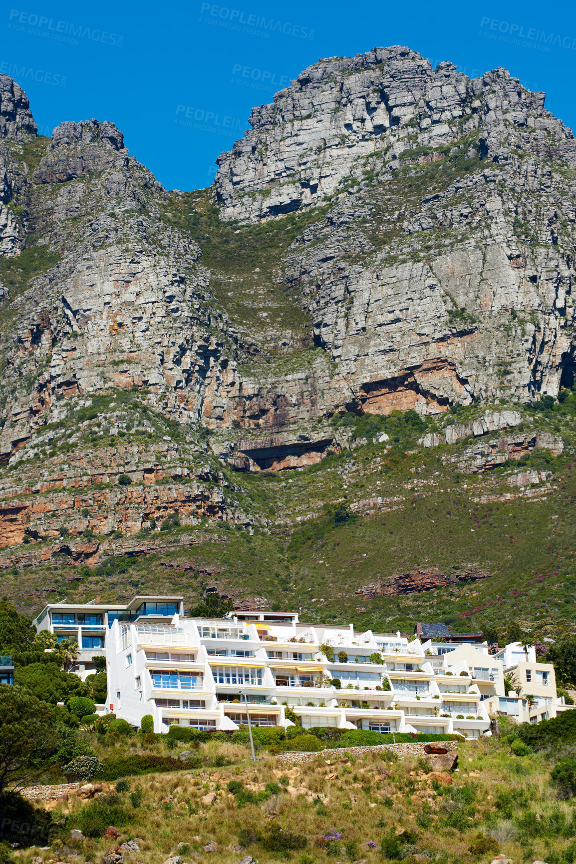Buy stock photo Low angle of Table Mountain near a vacation resort on sunny day in Cape Town, South Africa. Below view of a rocky mountaintop with greenery against blue sky. Background of popular tourist destination