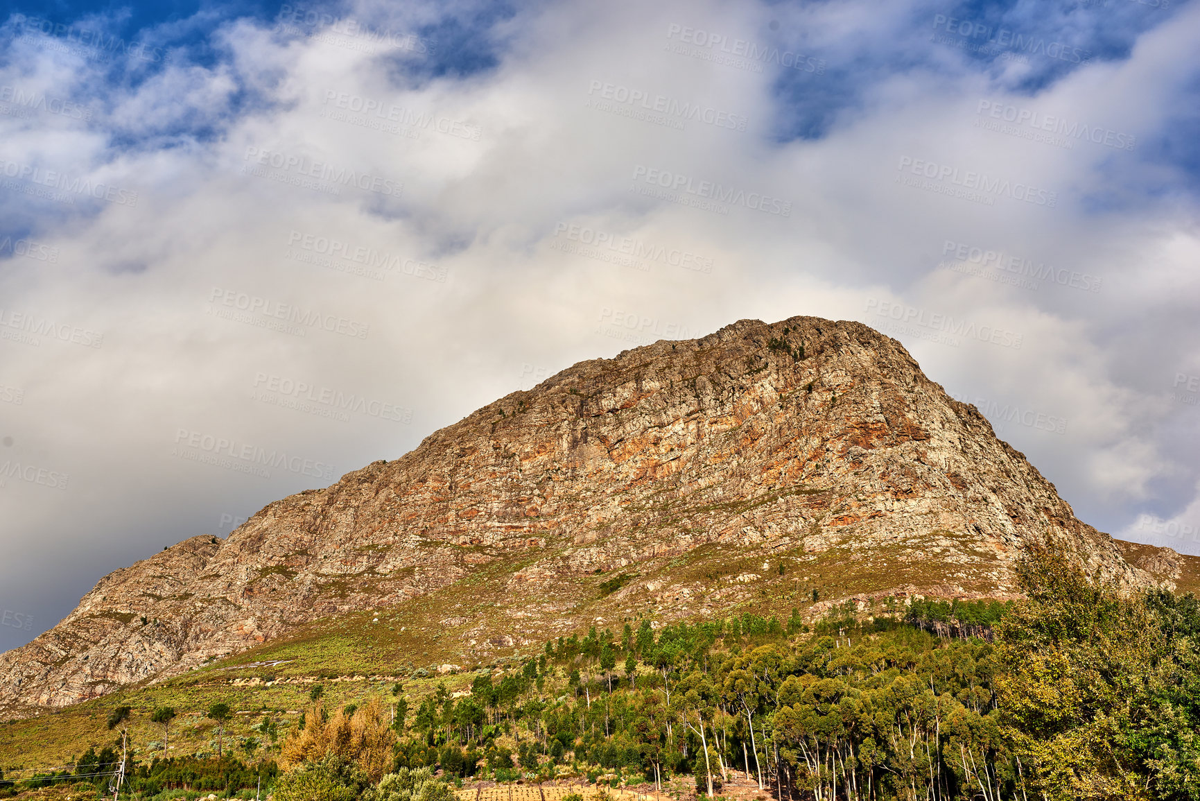 Buy stock photo A bottom view picture of Table mountain. A beautiful nature view of a high mountain shaped like a lion's head with forest, and a cloudy sky in the background. Copy space with scenic landscape view