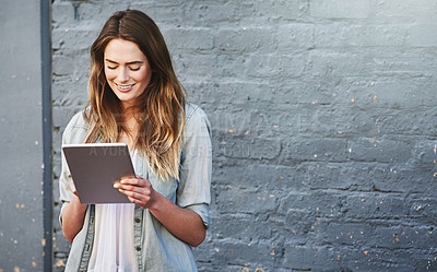 Buy stock photo Shot of a young woman standing outdoors and using a digital tablet against a gray wall