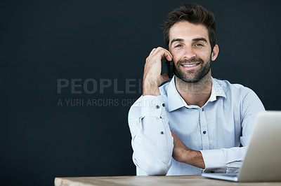 Buy stock photo Portrait of a young corporate businessman sitting at a desk against a dark background