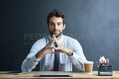 Buy stock photo Portrait of a young corporate businessman sitting at a desk against a dark background