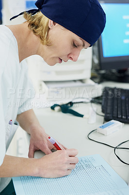 Buy stock photo Shot of a young surgeon filling out paperwork in a hospital