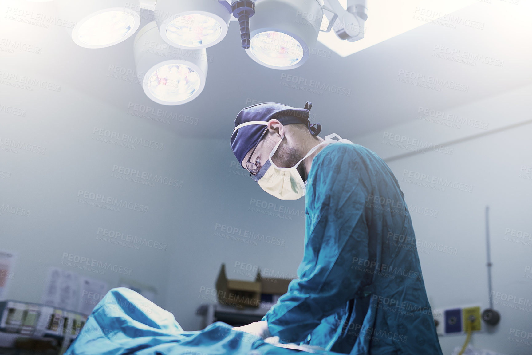 Buy stock photo Shot of a focused young surgeon performing surgery on a patient in an operating room