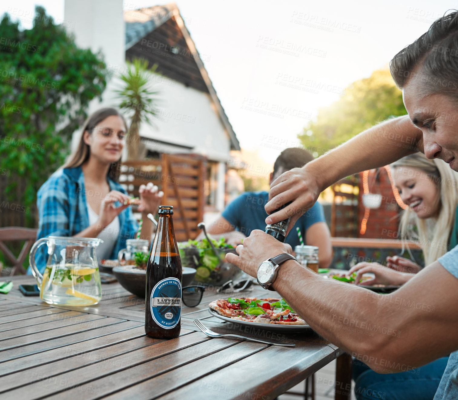Buy stock photo Shot of a young group of friends enjoying a meal together while sitting outside around a table in a garden