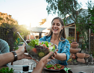 Buy stock photo Shot of young woman taking a salad bowl from a friend while being seated around a table outside in a garden