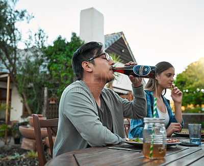 Buy stock photo Shot of a young man having a sip of a beer while being seated outside around a table with friends