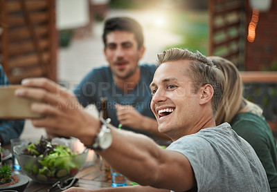 Buy stock photo Shot of a group of young friends getting closer for a self portrait while being seated outside around a table