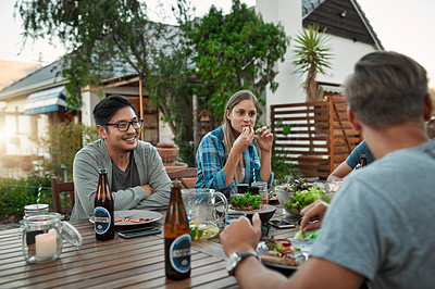 Buy stock photo Shot of a young group of friends enjoying a meal together while sitting outside around a table in a garden