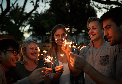 Buy stock photo Shot of a group of cheerful young friends having fun with sparklers together outside at night