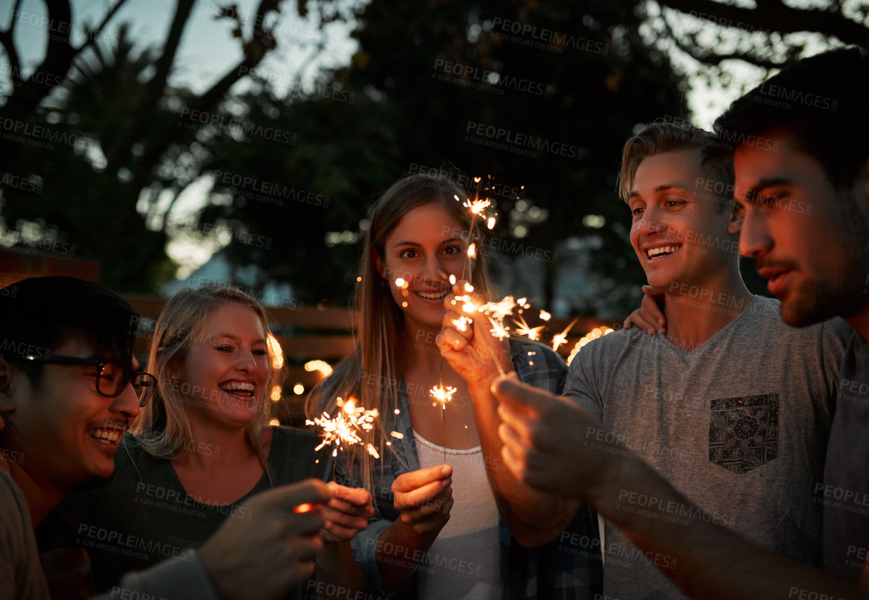 Buy stock photo Shot of a group of cheerful young friends having fun with sparklers together outside at night