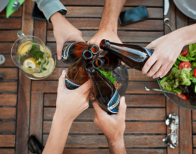 Buy stock photo High angle shot of a group unrecognizable people's hands holding beer bottles and toasting outside around a table